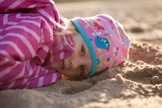Cute little girl lying in sand on the beach
