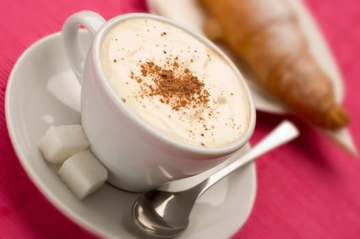 cup of cappuccino with croissant close up on pink
