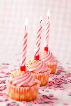 Close-up of pink muffins with party candles. Studio shot.