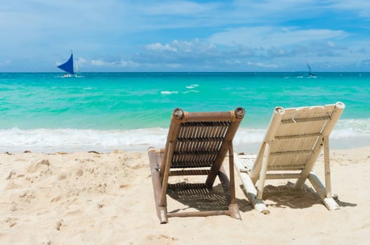 tropical beach with two beach chairs facing the blue sea