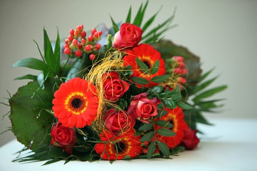 Colourful floral bouquet of orangey-red flowers in green foliage lying on a tabletop.
