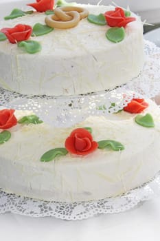 Two-layered wedding cake decorated with orangey red rose buds and intertwined wedding rings.