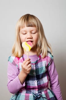 Cute little girl with a heart shape lollipop. Studio shot.