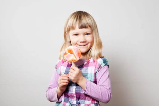 Cute little girl with a big orange lollipop. Studio shot.