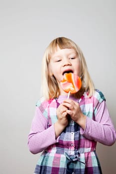 Cute little girl with a big orange lollipop. Studio shot.
