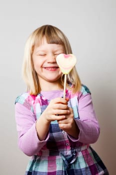 Cute little girl with a heart shape lollipop. Studio shot.