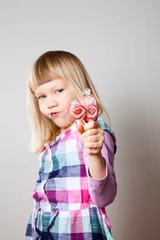 Cute little girl with heart shape lollipops. Studio shot.
