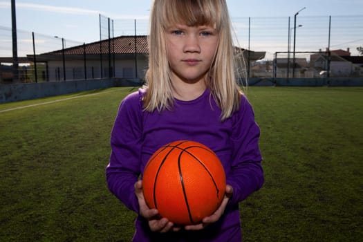Little girl standing with a basketball on an outdoor court