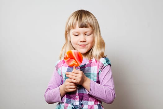 Cute little girl with a big orange lollipop. Studio shot.