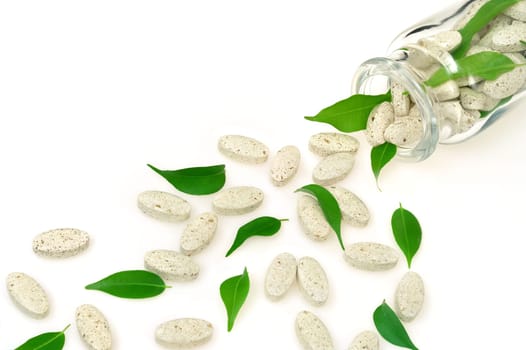 Herbal supplement pills and fresh leaves spilling out of bottle - alternative medicine concept