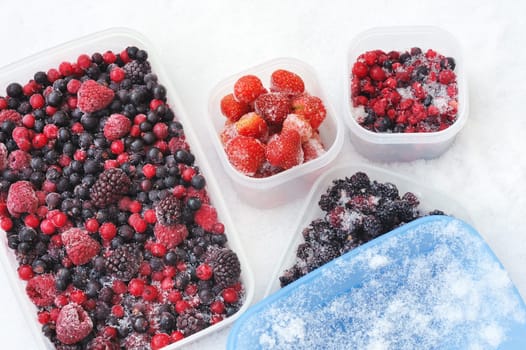 Plastic containers of frozen mixed berries in snow - red currant, cranberry, raspberry, blackberry, bilberry, blueberry, black currant, strawberry