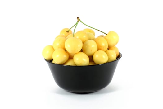 Yellow cherry in a black bowl isolated on white