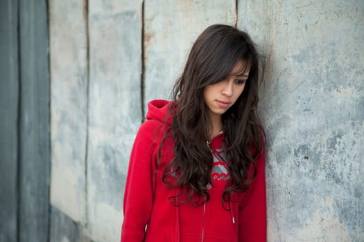 Teenage girl leaning against grunge wall with expression of sadness.