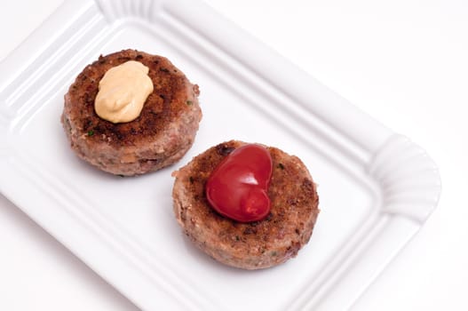 Two meatballs on a plate with mustard and ketchup