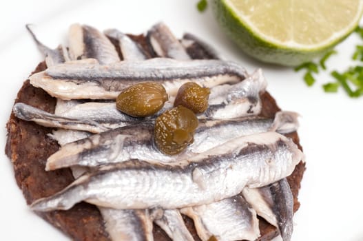 A canape of wholemeal bread with small anchovies and capers and a lime and chives