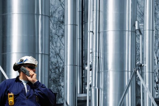 engineer, worker, talking in phone, large oil, gas and fuel pipes inside refinery
