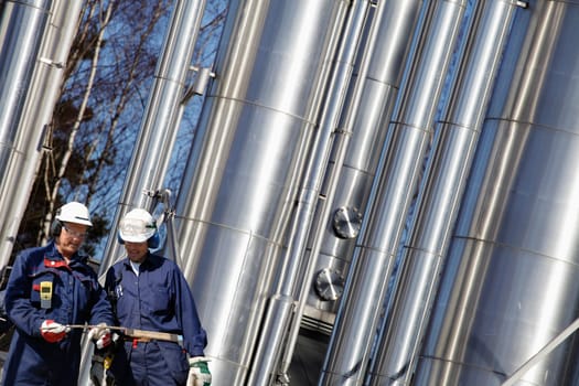 two gas and oil workers with large shiney pipelines in background