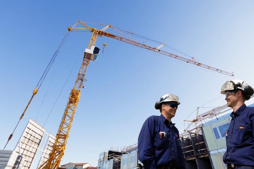 two construction-workers with cranes and scaffolding in background