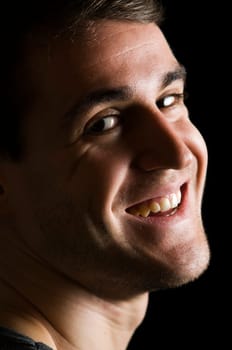 Close side head portrait of a young man in partial shade against a black background looking contentedly at the camera
