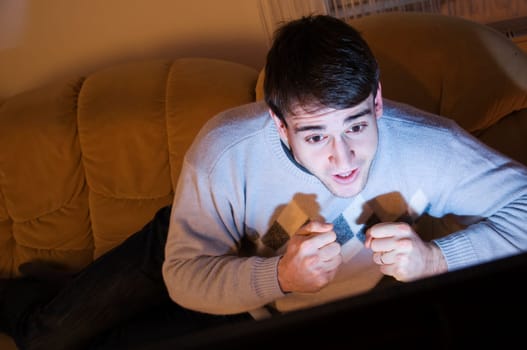 Young man with short brown hair lying tensely on the sofa in front of the TV