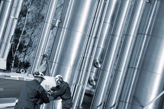 gas workers with pipeline machinery, large shiney gas pipes in background