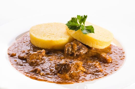 Fresh goulash with polenta on white plate close up