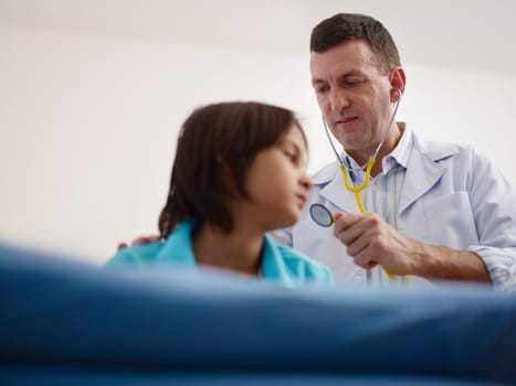 Friendly caucasian doctor working and visiting with stethoscope sick child in medical office. Focus on foreground