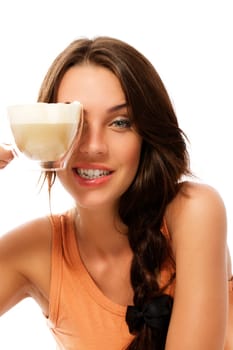 Pretty woman holding cup with cappuccino coffee in front of her eye in front of white background