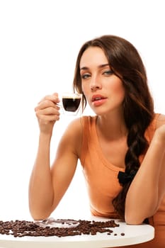 Beautiful young woman sitting at a table with a cup of espresso coffee against white background