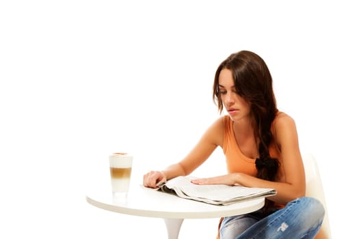 Young woman sitting at a table with latte macchiato and reading newspaper against white background