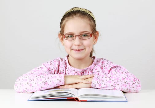 Cute schoolgirl with glasses reading book
