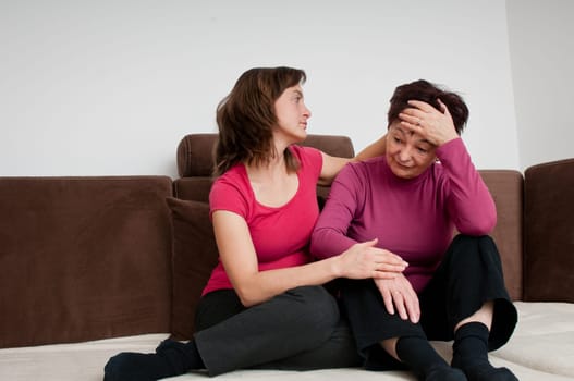 Daughter (young woman) comforts her depressed senior mother at home