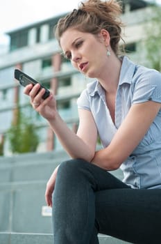 Young unhappy woman typing on mobile phone - outdoors in street