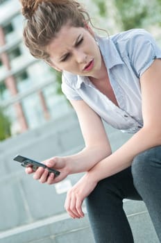 Young worried woman with unhappy expression holding mobile phone - outdoors in urban setting