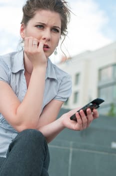 Young worried woman with unhappy expression holding mobile phone - outdoors in urban setting