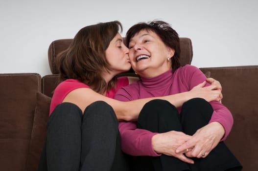 Portrait of daughter kissing happy senior mother sitting on sofa at home