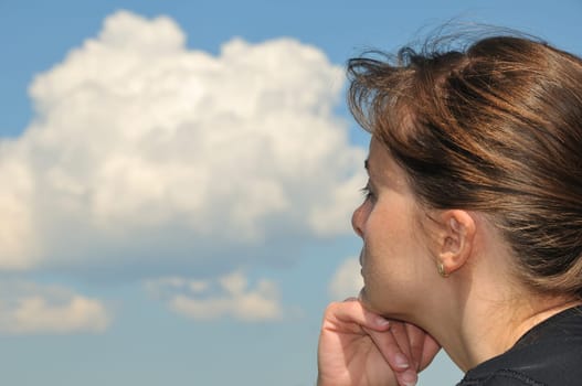 Head of Young woman dreaming in day with blue sky and white clouds in background - detail