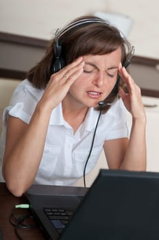 Young business person with headache working with computer(headset on head)