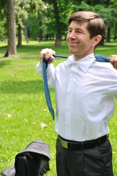 Escape from civilization - senior business man putting off tie and relaxing in fresh green park