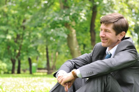 Senior people series - smiling mature business man siting on green grass and relaxing in park