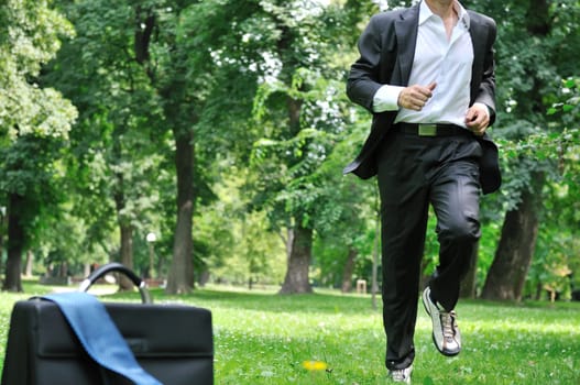 Training - business man running in park, bag and tie laid on grass