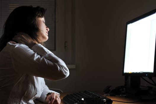 Neck pain - young tired business woman working overtime at computer, night setting