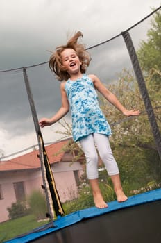 Small cute child jumping on trampoline - garden and family house in background