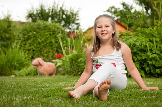 Backyard portrait of smiling child (nine years old girl) sitting on grass