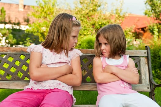 Small girls (sisters) siting on bench offended after quarrel - outdoors in backyard