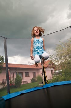Small cute child jumping on trampoline - garden and family house in background