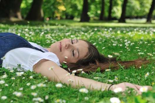 Relaxed young person (teenage girl) lying in grass and flowers with stretched hand - closed eyes