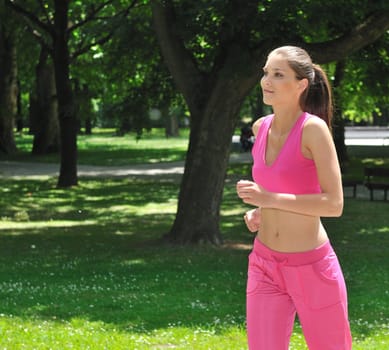 Young beautiful woman in pink running (jogging) outdoors in park on sunny day
