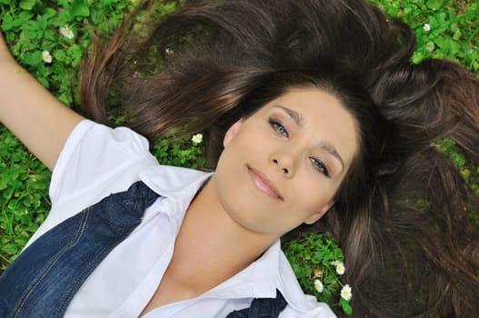Detail of cheerful happy teenage girl lying in fresh green grass with flowers