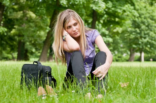Young worried business woman siting in grass - notebook bag and shoes lying next